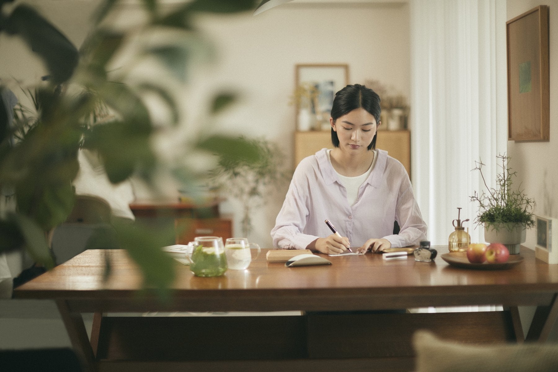 木製ダイニングテーブルで手紙を書く女性の生活シーン。テーブルにはインク瓶やペンとともにLefumeも置かれている