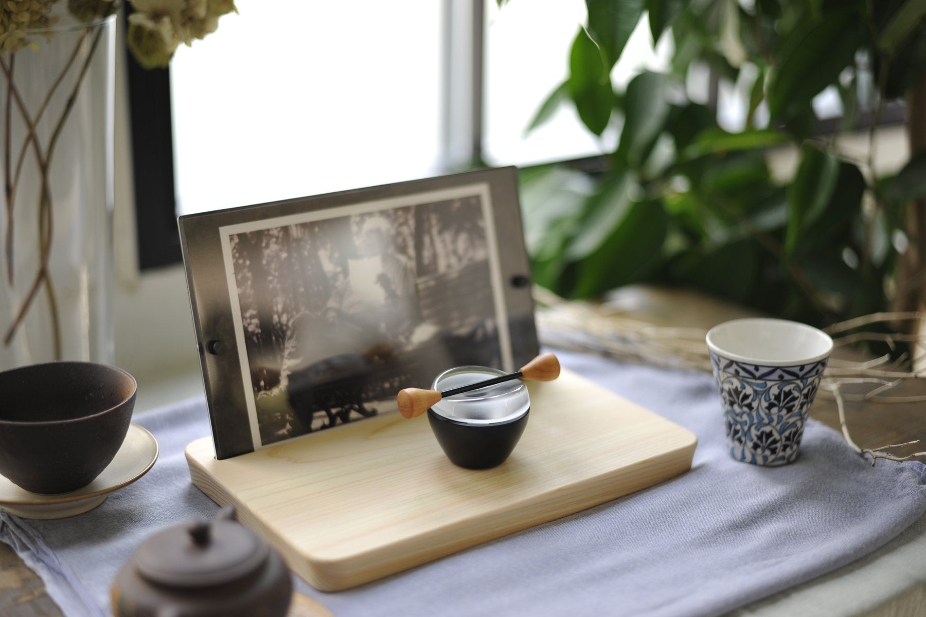 木製トレーの上で、モノクロ写真を挟んだPicstalと、黒色のCaprinを並べた生活シーン。器やカップとともに