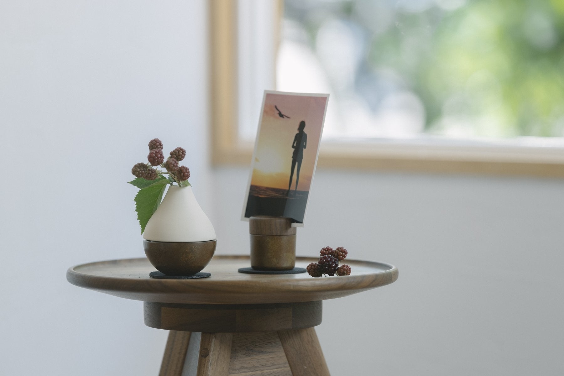 木製の丸テーブルの上に、白色のPictuary Cylinderと写真立てを置き、ベリーの枝を飾った生活シーン
