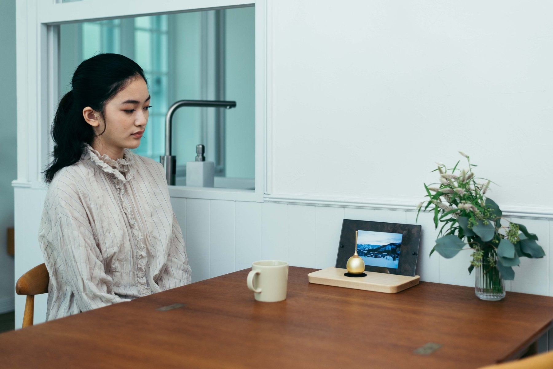 ダイニングテーブルで女性が座る奥に、写真立てと金色のCherin Miniを置いた生活シーン