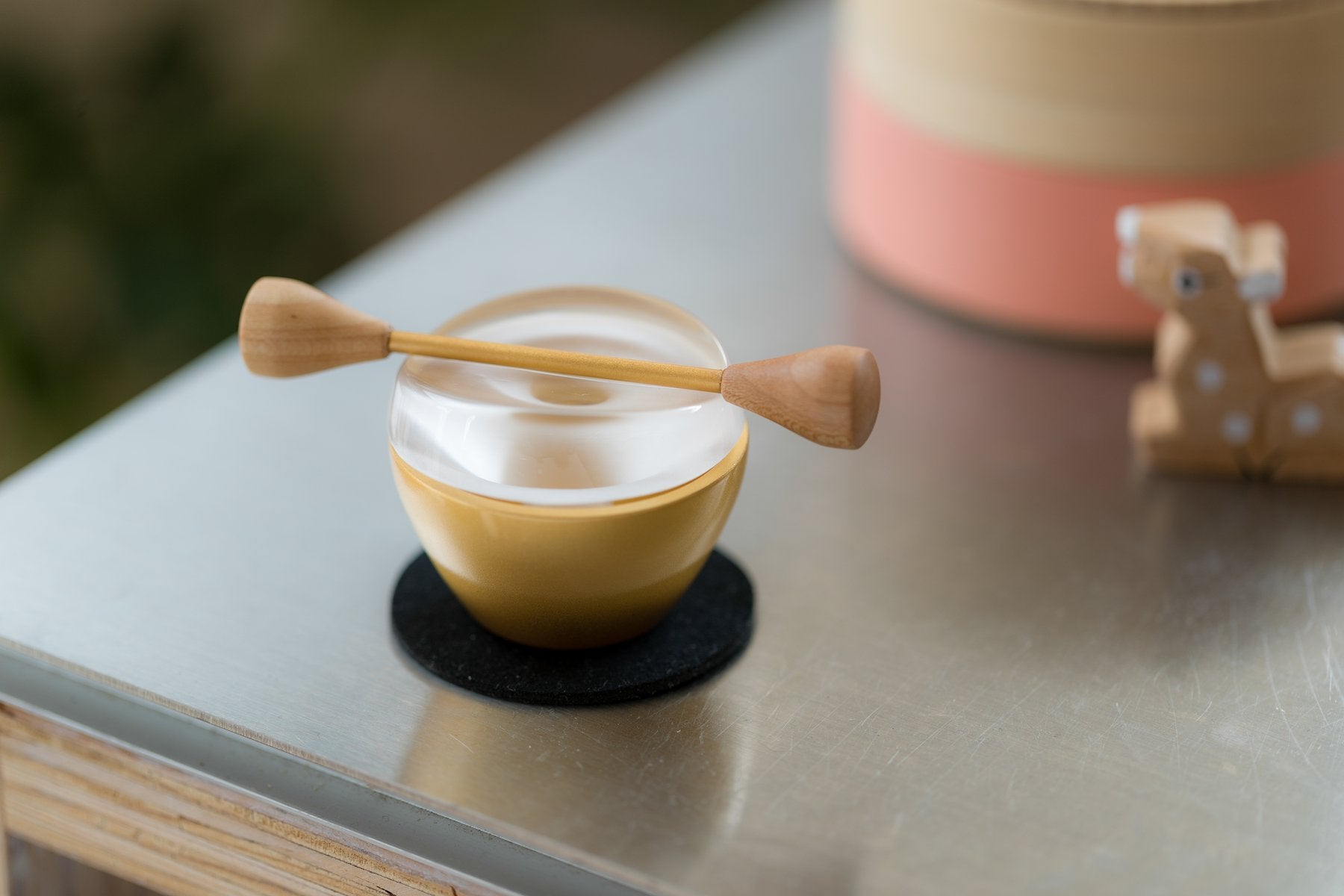 ガラスの丸い蓋にリン棒を渡した金色のPaddle本体を黒いコースターの上でクローズアップした一枚