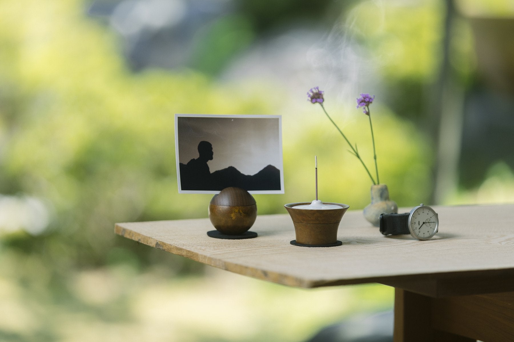 木製テーブルの上で、写真立てとして使ったPictuary Sphere(茶色)と線香を立てた同色の器、花瓶、腕時計を並べた屋外の生活シーン
