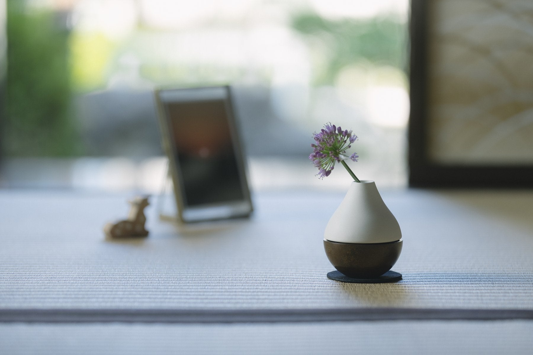 畳の上でりん棒を花器に近づけている手元。白磁のポタリンと写真立てが写る