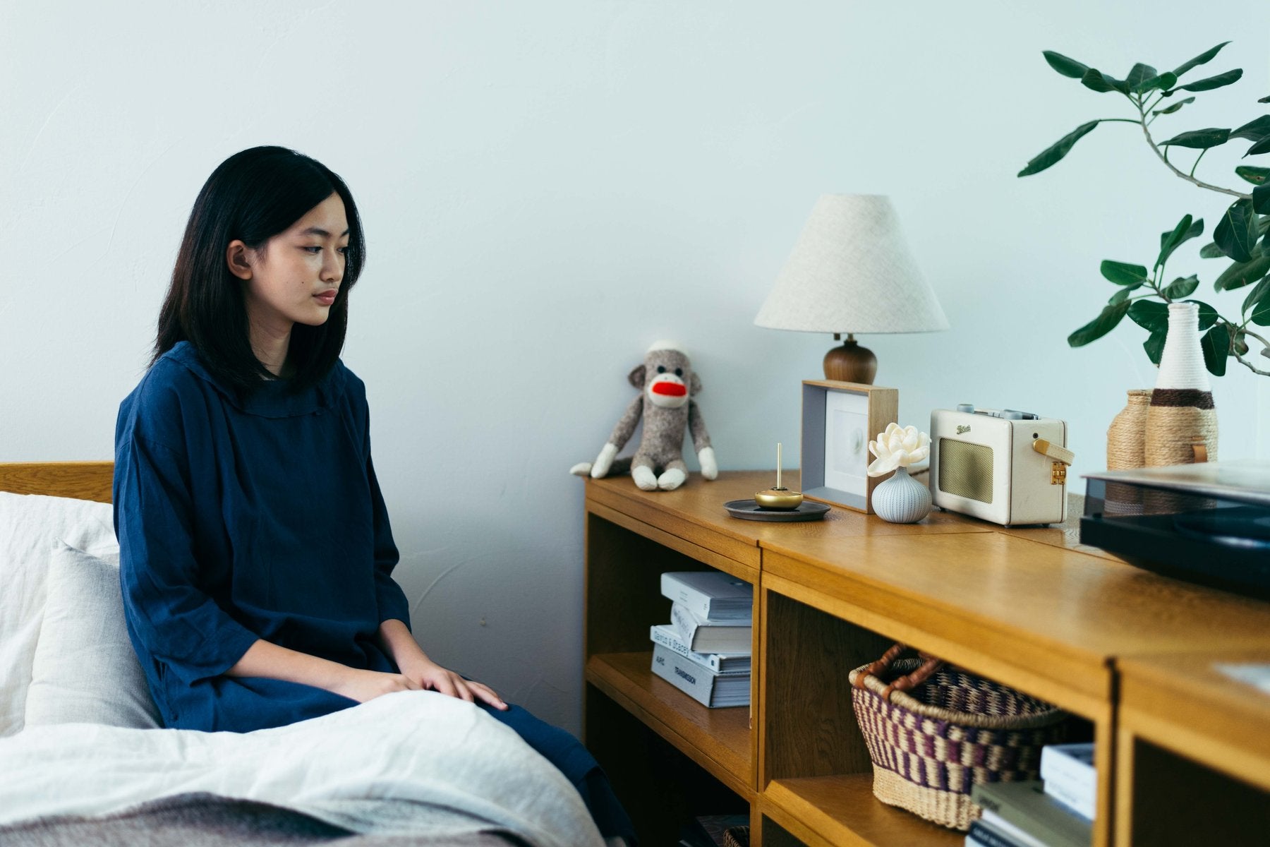 寝室でベッドに座る女性の奥、木製キャビネットの上に金色のRingを置いた部屋全体が見える生活シーン